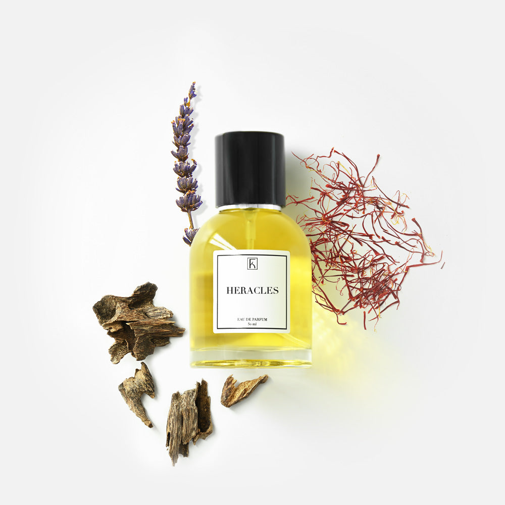 Ein Parfümflakon mit der Aufschrift "Heracles", daneben Lavendelblüten, getrocknete Holzstücke und rote Safranfäden.
