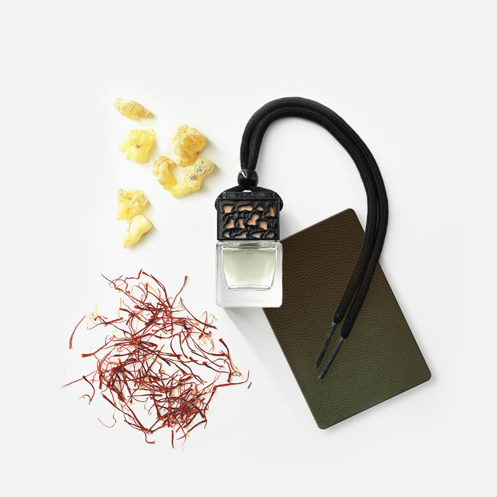 Ein kleines Glasfläschchen mit schwarzem Deckel und Band, daneben braune Karte, gelbe Harzstücke und rote Safranfäden.