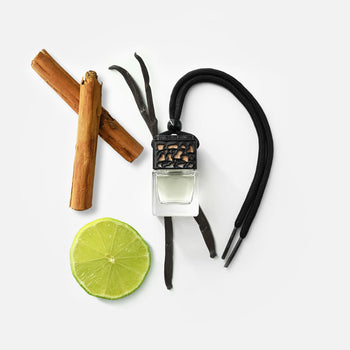 Ein kleiner Glasflakon mit schwarzem Verschluss und Kordel, daneben eine halbe Limettenscheibe, zwei Zimtstangen und zwei Vanilleschoten.
